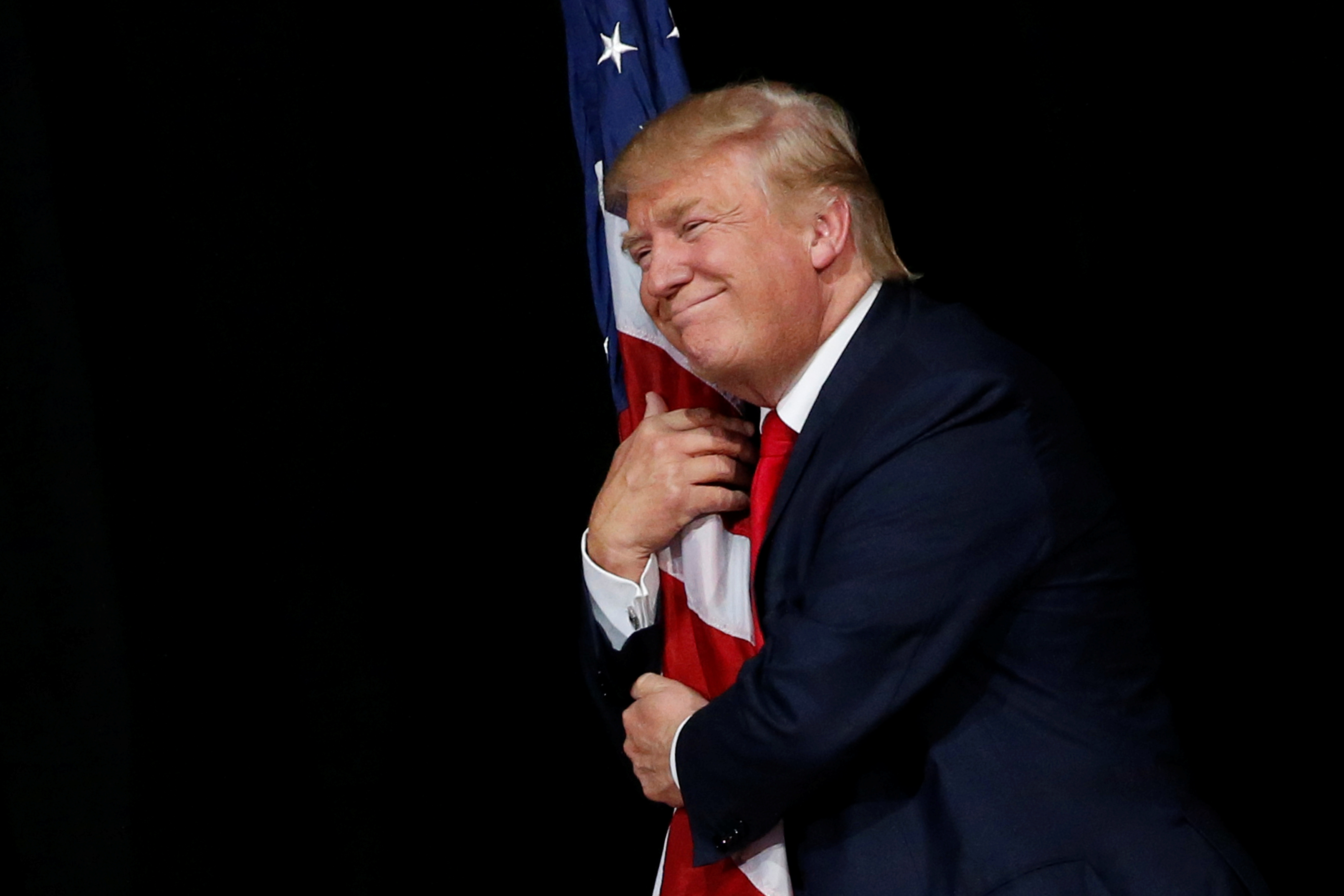 Trump hugs a U.S. flag as he comes onstage to rally with supporters in Tampa, Florida